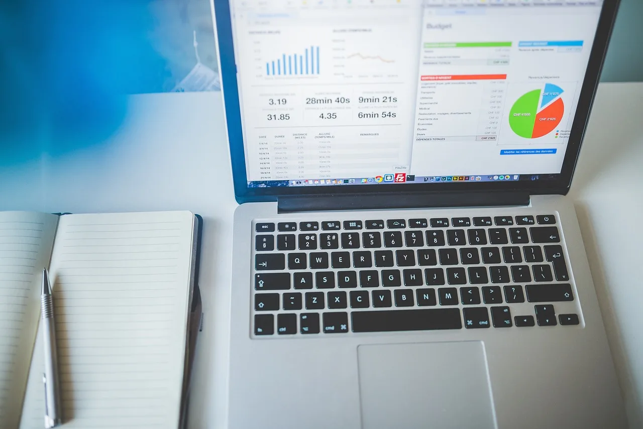 Laptop showing marketing analytics charts beside an open notebook, used for planning a small business digital marketing budget Laptop showing marketing analytics charts beside an open notebook, used for planning a small business digital marketing budget