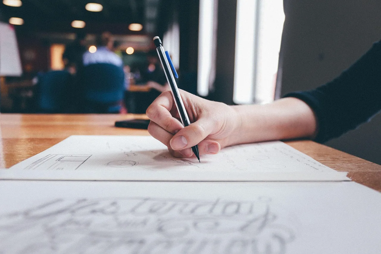 Hand writing and sketching a plan on paper at a desk, drafting a software requirements brief Hand writing and sketching a plan on paper at a desk, drafting a software requirements brief